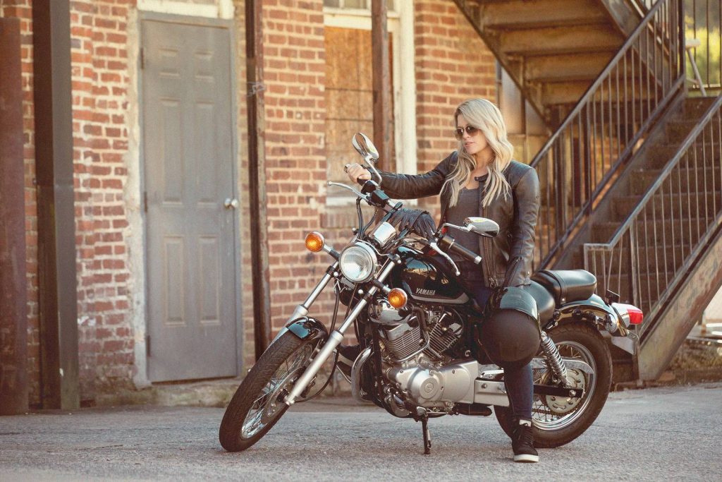 Woman sitting on Yamaha V-Star 250 in front of brick building