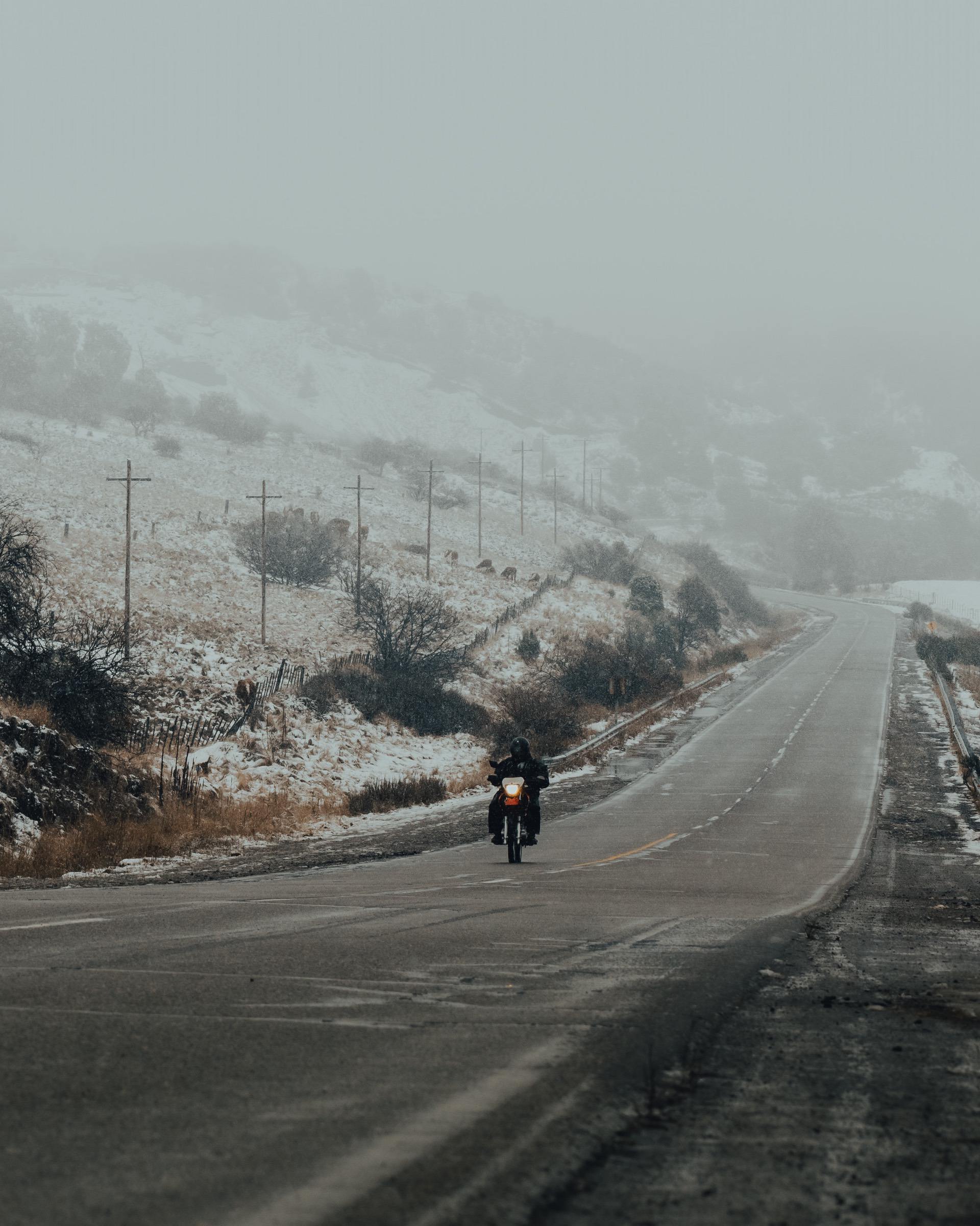 Motorcyclist riding in challenging conditions with snow near highway