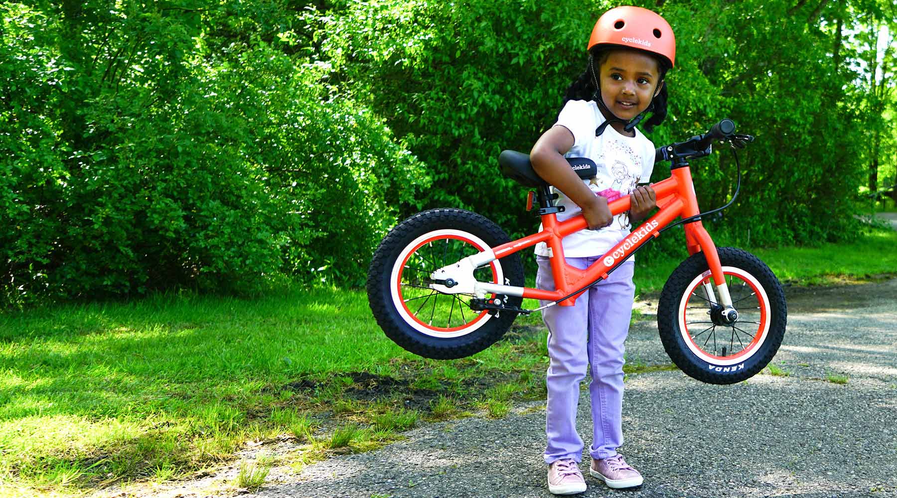 Young child holds up her kids bike with both hands during day time