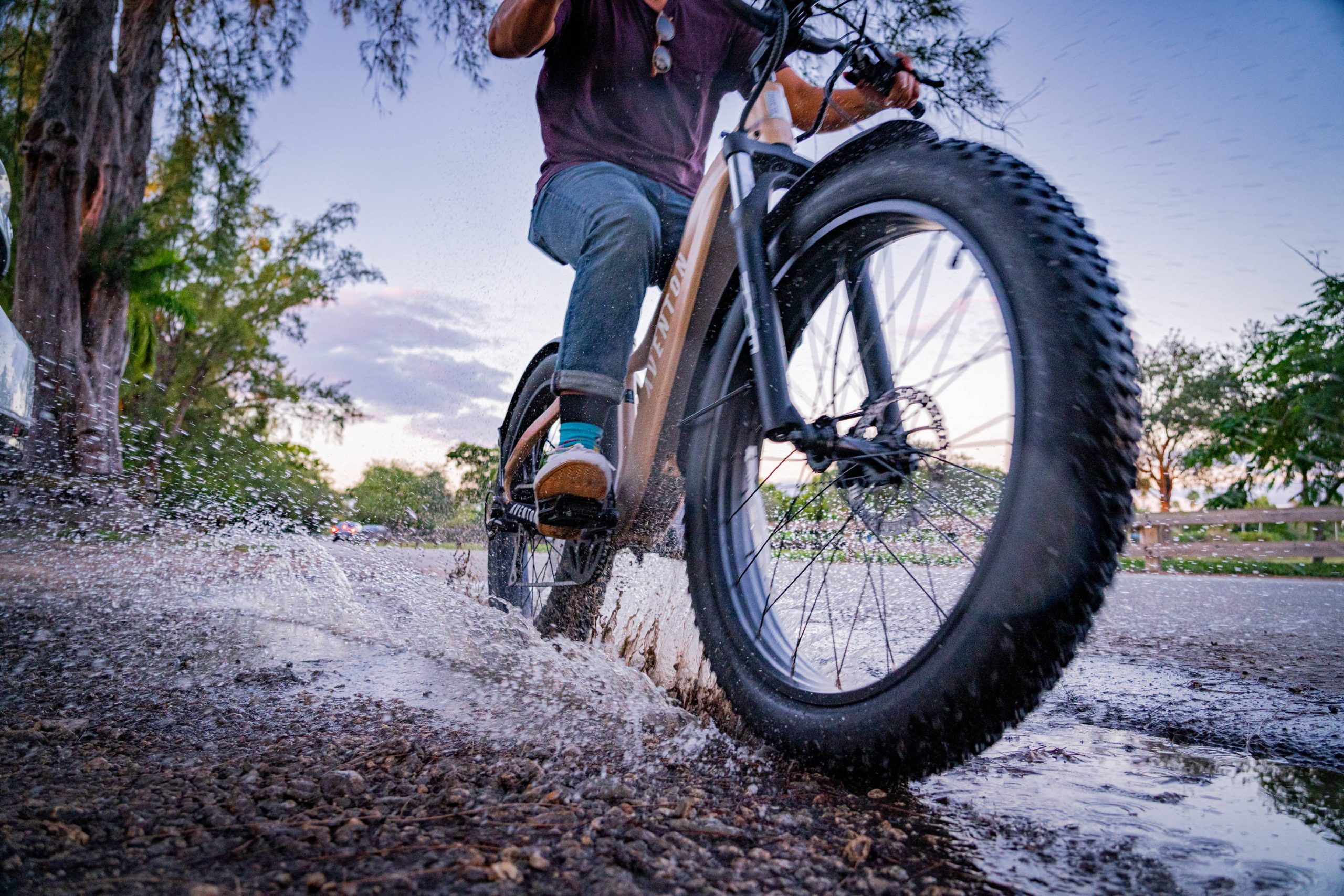 Close up shot of cyclist riding fat-tire Aventon eBike through a puddle at speed on the roadside