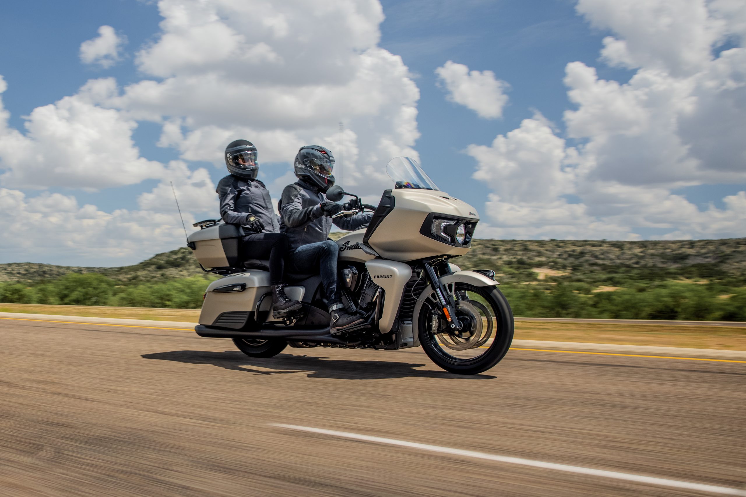 An image of a rider and passenger cruising down a road on the Indian Pursuit Dark Horse.