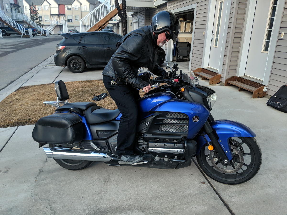 Motorcyclist mounting motorcycle now with right foot on peg